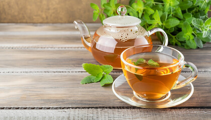 Tea in a transparent cup and teapot from fresh melissa leaves on a wooden background. Traditional herbal drink. Horizontal frame. Copy space