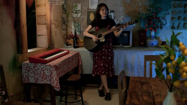 Cute and young Asian woman singing and playing guitar at home, Long shot