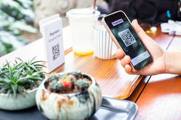Customer hand using smart phone to scan Qr code payment tag with blur coffee on wooden table to...