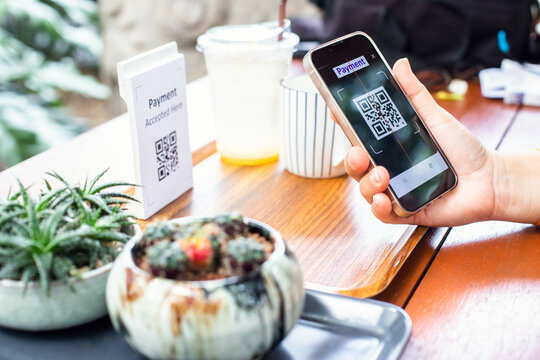 Customer hand using smart phone to scan Qr code payment tag with blur coffee on wooden table to accepted generate digital pay without money. Qr code payment concept. - Powered by Adobe