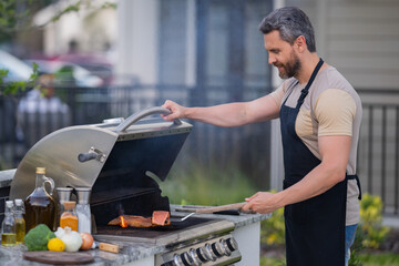 Male chef grilling and barbequing in garden. Barbecue outdoor garden party. Handsome man preparing barbecue meat. Concept of eating and cooking outdoor during summer time.