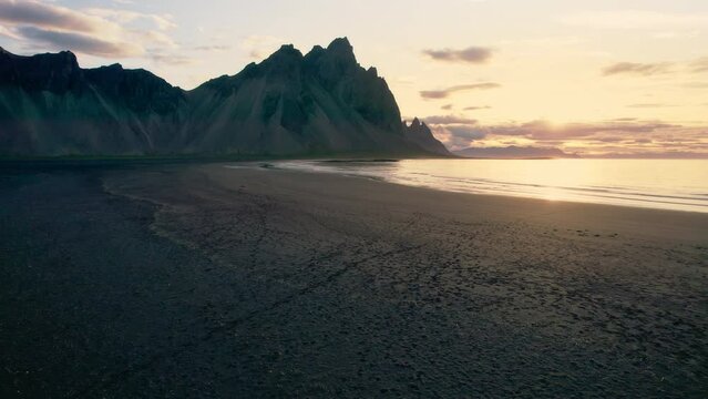 Sunrise over Vestrahorn mountain and man traveler walking on black sand beach in Stokksnes peninsula