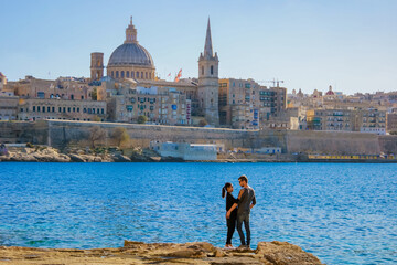 A couple on a city trip to Valletta Malta city Skyline, colorful house balcony Malta Valletta, panoramic view over Valletta Malta old town at sunset - obrazy, fototapety, plakaty