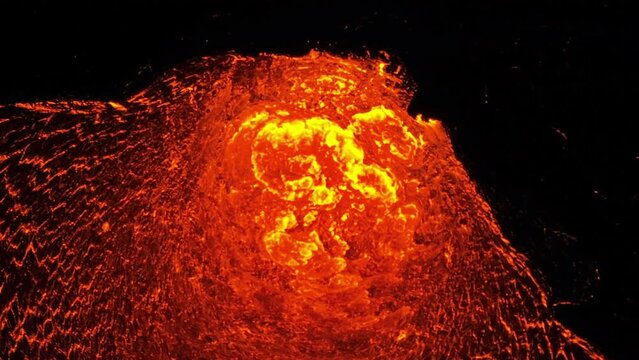 Aerial zoom shot of glowing magma coming through a crater fume in earths surface