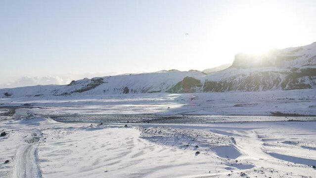 Aerial shot of a parachuters silhouette coming in to land in a snowy valley in Iceland