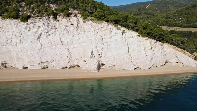 Aerial view from the sea on the coast revealing a green landscape behind the cliff. Flying back from the coast. Gabbiani, Italy. 