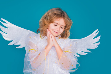 Cute angel kid, studio portrait. Blonde curly little angel child with angels wings, isolated background. Dreamy angel kids face. Daydreamer child portrait close up. Dreams and imagination.