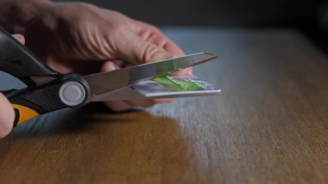 A man cuts a credit card with scissors. Destruction of inactive bank cards in order to increase financial security.