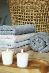Fototapeta na wymiar A stack of gray and beige terry towels next to candles and a wicker basket