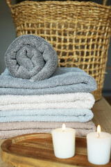 Obraz na płótnie Canvas A stack of gray and beige terry towels next to candles and a wicker basket