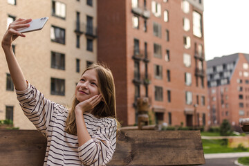 Fototapeta premium Beauty Teen girl takes a selfie on the phone on the street among brick houses