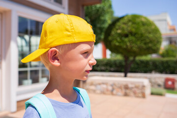 A little boy of Caucasian in a school uniform with a backpack looks at the road in the school yard. Concept back to school. Elementary school, developing activities for preschoolers. Space for text