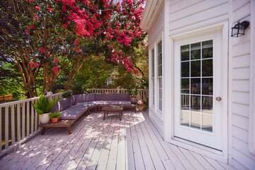 wooden terrace covered in beautiful flower petals under the blooming crape myrtle tree. lounge zone on the summer patio - obrazy, fototapety, plakaty