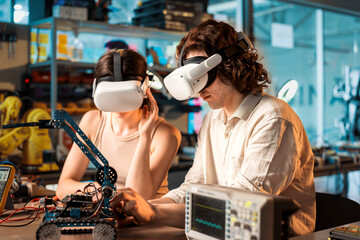 Young man and woman in VR glasses doing experiments in robotics in a laboratory