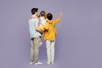 Full body back rear view young parents mom dad child kid girl 6 years old wearing blue yellow casual clothes hold daughter point finger aside isolated on plain purple background. Family day concept.