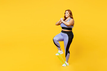 Fototapeta na wymiar Full body side view young chubby plus size big fat fit woman wear blue top warm up training use rubber elastic bands for legs isolated on plain yellow background studio home gym Workout sport concept