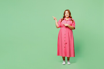 Full body smiling cheerful fun young chubby redhead woman wear casual clothes pink dress point index finger on area copy space isolated on plain pastel light green color background. Lifesyle concept.