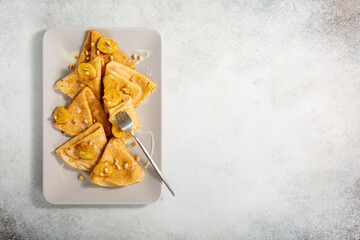 Crepes on rectangular plate on gray background. Thin pancakes served with bananas, pine nuts and sweet sauce. Top view. Copy space.