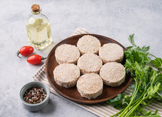 Chicken meat cutlets, not cooked, raw, on a wooden plate on a light background with fresh herbs and tomatoes. Delicious homemade diet food