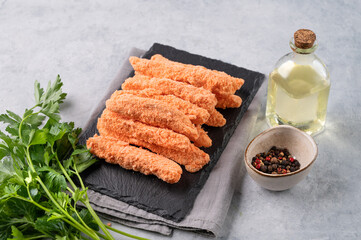 Fish fillet sticks, raw, not fried on a slate board with parsley on a light background with oil and spices. Diet and healthy food