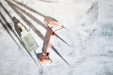 Skin care cosmetics, marble facial massager and cosmetic oil or serum on a gray background under the shadow of a palm tree