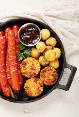 Grilled meat sausages in a pan with vegetables.