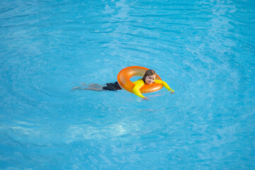 Swimming, summer vacation. Cute child playing in blue water. Kid enjoying summer vacation in water in the swimming pool. Cute little kid in swimming suit relaxing on an inflatable ring. Kid floating