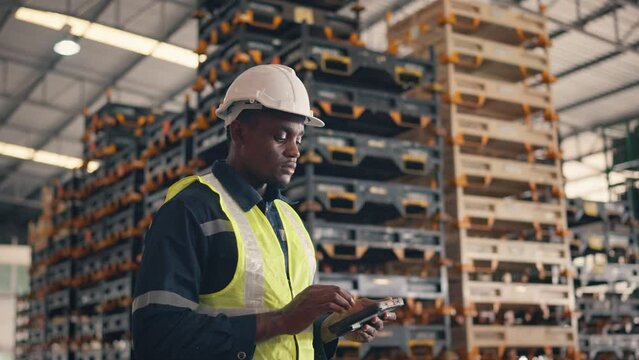 African American man worker checks products stock inventory with digital tablet in the retail warehouse full of shelves Male employee wearing hard hat doing work in storehouse.