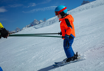 Profile view of child learn to ski with instructor holding poles