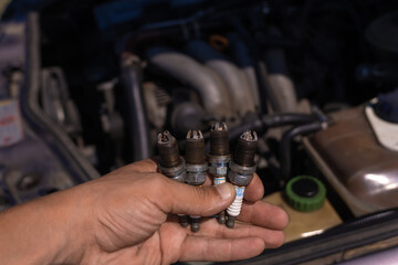 Close-up of a hand with four used car candles on the background of the engine. Concept of car repair