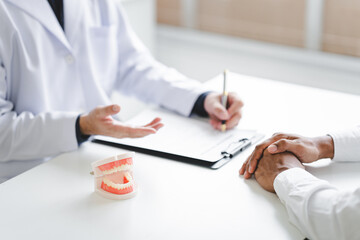 Dentist explaining endodontic treatment to patient in office Dentist holding a tooth model for...