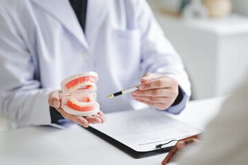 Dentist explaining endodontic treatment to patient in office Dentist holding a tooth model for examination and research