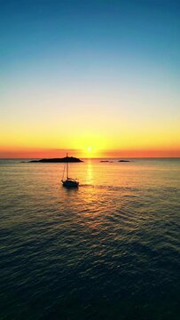 Reflejo de la salida del sol en el océano con isla y barco velero, DJI, toma lineal