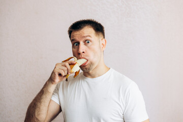 A guy in a white T-shirt holds a ripe yellow banana and eats it. Summer fruits from the garden