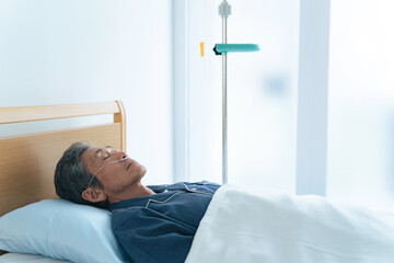酸素チューブをつけてベッドに寝るシニア男性