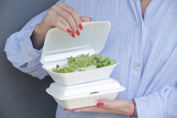 Woman's hands holding open takeaway foam lunch box with healthy fresh green salad in it.	
