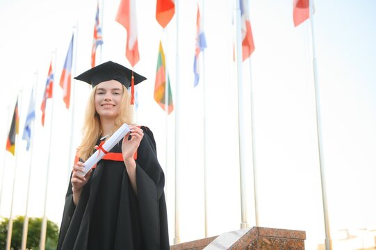 Happy university graduate girl. The girl is standing near the university against the background of the flags of different countries. The concept of international education.