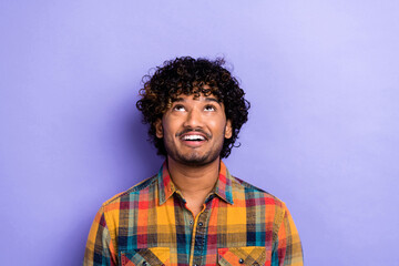 Photo of young man curly hair wearing plaid trendy shirt looking interested above his head empty space isolated on purple color background