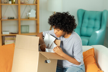 African girl unpacking delivery looking in box. Happy woman opening carton box. Female getting...