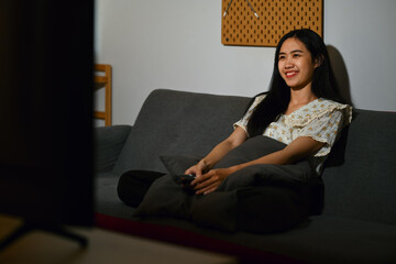 Smiling young Asian woman watching romantic movie on TV at home in evening alone.