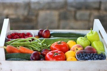 Wooden crate full of healthy seasonal fruit and vegetable, in the garden. Selective focus.