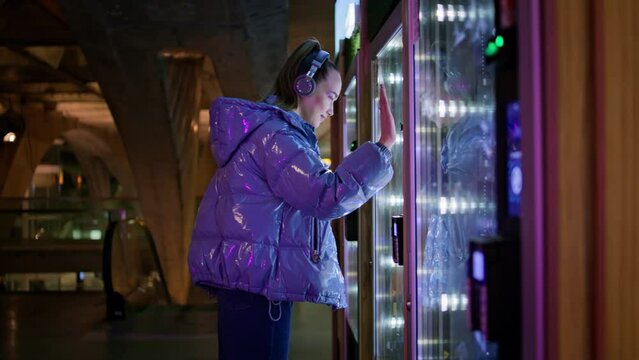Woman buying snacks vending machine at subway late evening. Girl make purchase.