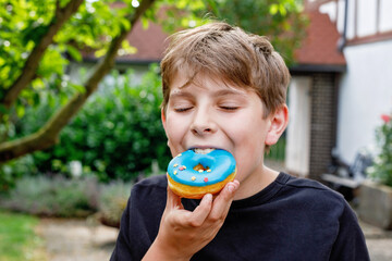 Preteen kid boy eating sweet doughnut in summer. Happy child with donut, unhealthy food.