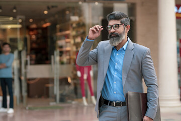 Confident Indian corporate man holding laptop in hand, walking on street side