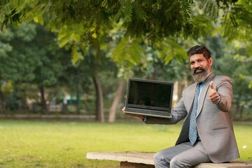 Obraz premium Indian businessman showing laptop screen and thumps up