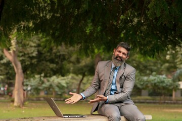 Obraz premium Indian businessman giving happy expression while looking in laptop at park.