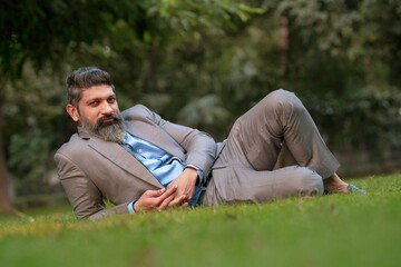 Naklejka na ściany i meble Indian businessman laying down at garden