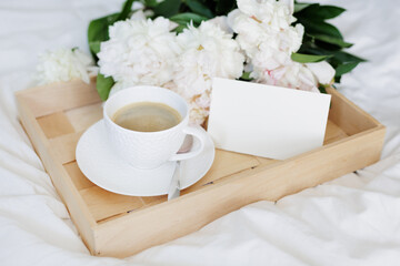 The atmosphere of a romantic morning, coffee in bed with peony flowers on tray with blank card