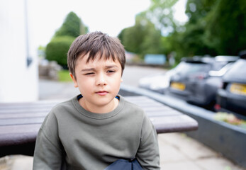 Portrait Young boy looking out deep in thought, School kid sitting  alone on wood beanch outside,...
