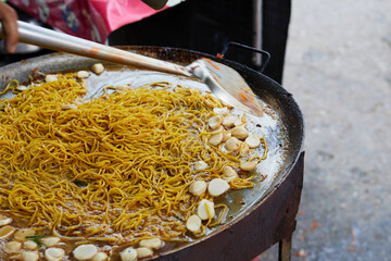 Cropped view of chef cooking the egg noodle and meatballs on a large flat pan